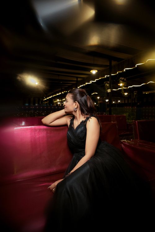 Free Beautiful woman in a black dress relaxing elegantly on a velvet sofa in a chic indoor setting. Stock Photo