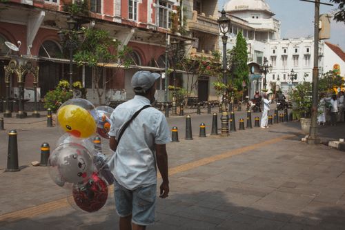 Free A street vendor with balloons walks along a historic building facade in an urban setting. Stock Photo