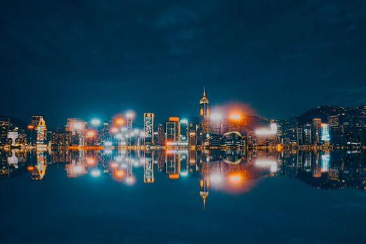 Vibrant Hong Kong skyline at night reflecting in water, showcasing city lights.