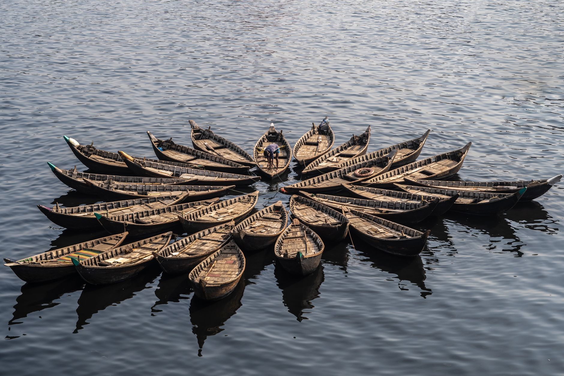 Aerial view of wooden boats arranged in a circular pattern on a calm water surface.