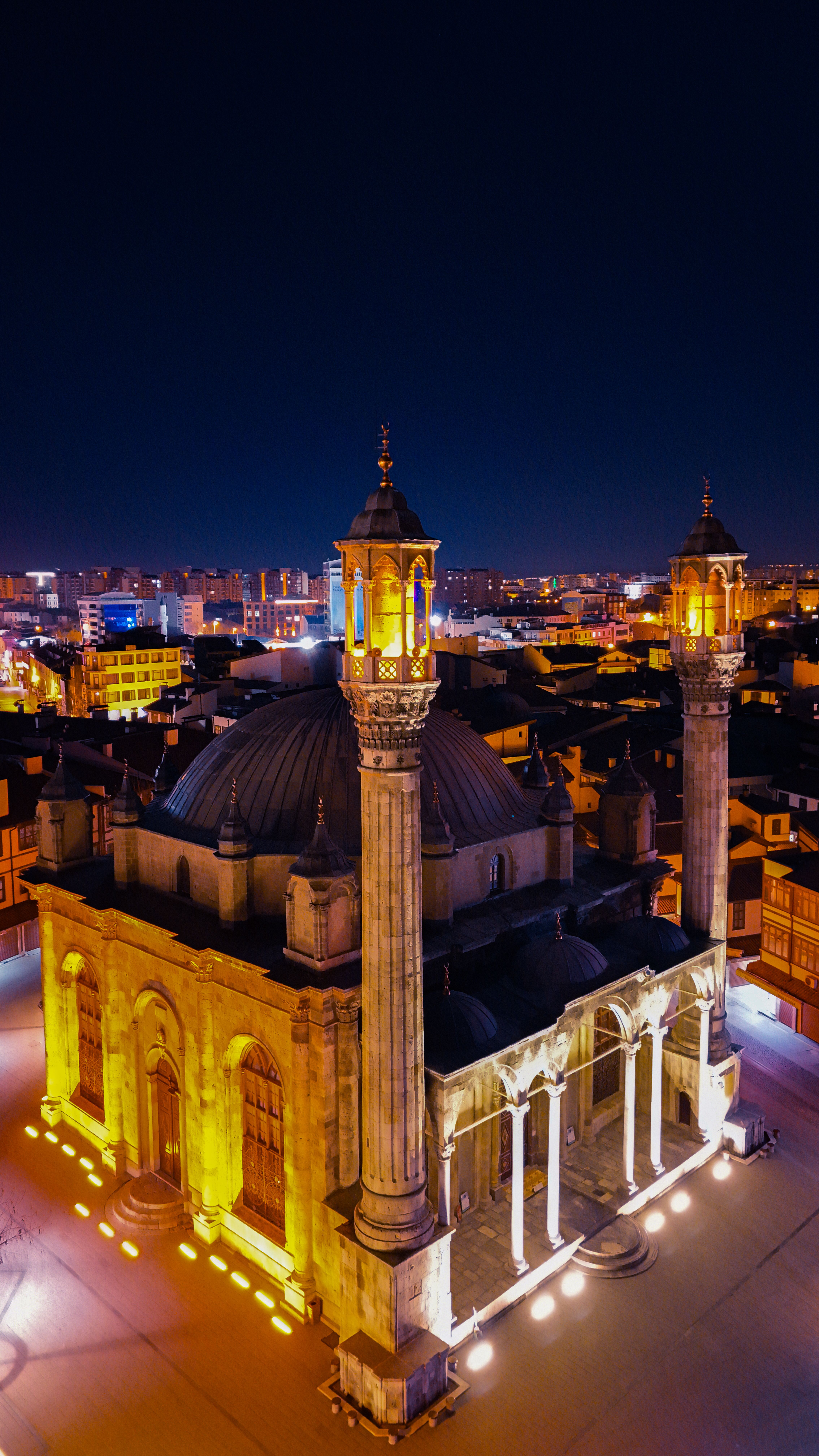 Aerial night view of a beautifully illuminated historic mosque in Konya, showcasing architectural elegance.