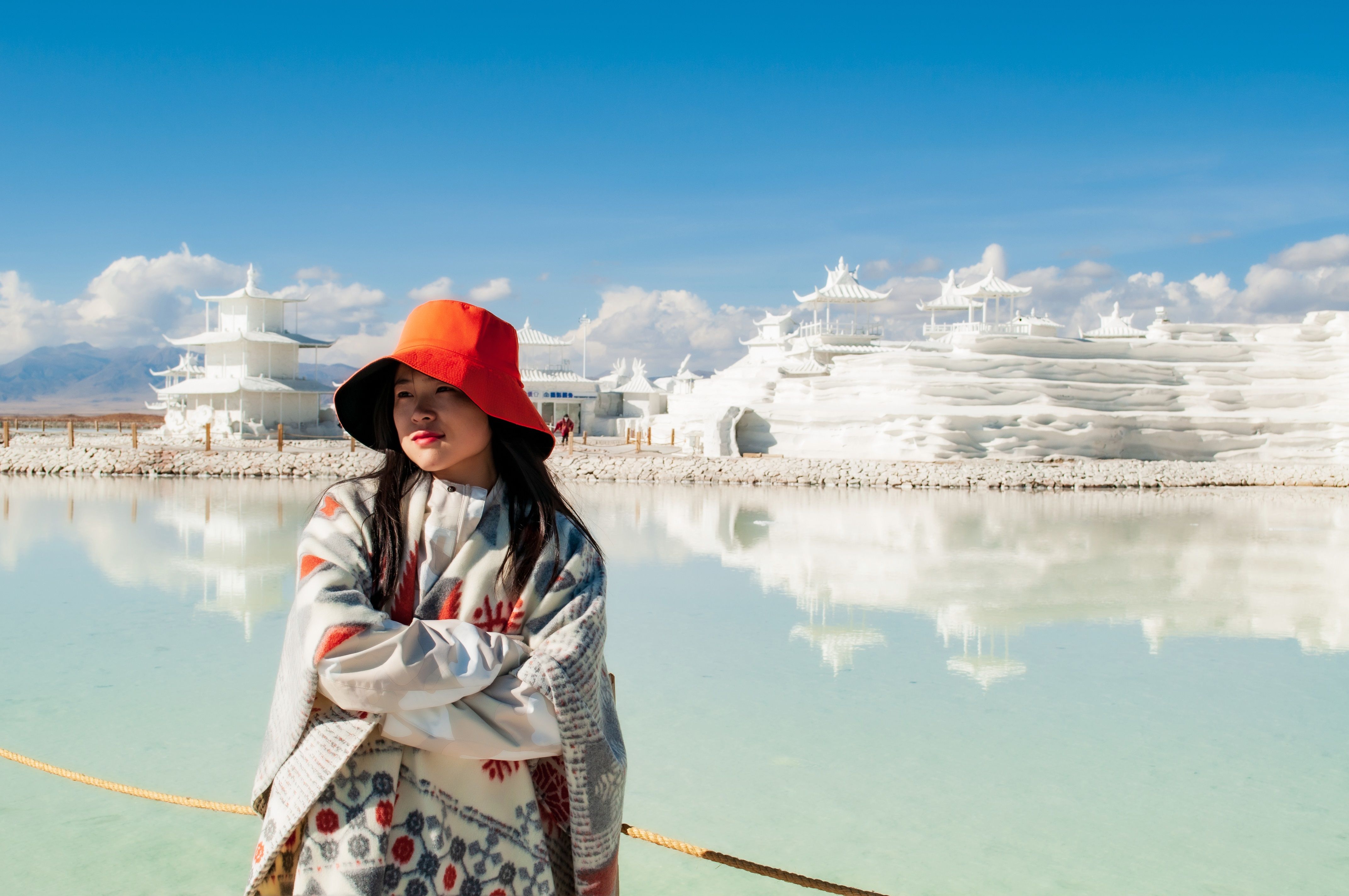 Woman stands in front of a white architectural wonder reflecting in the water under a clear blue sky.