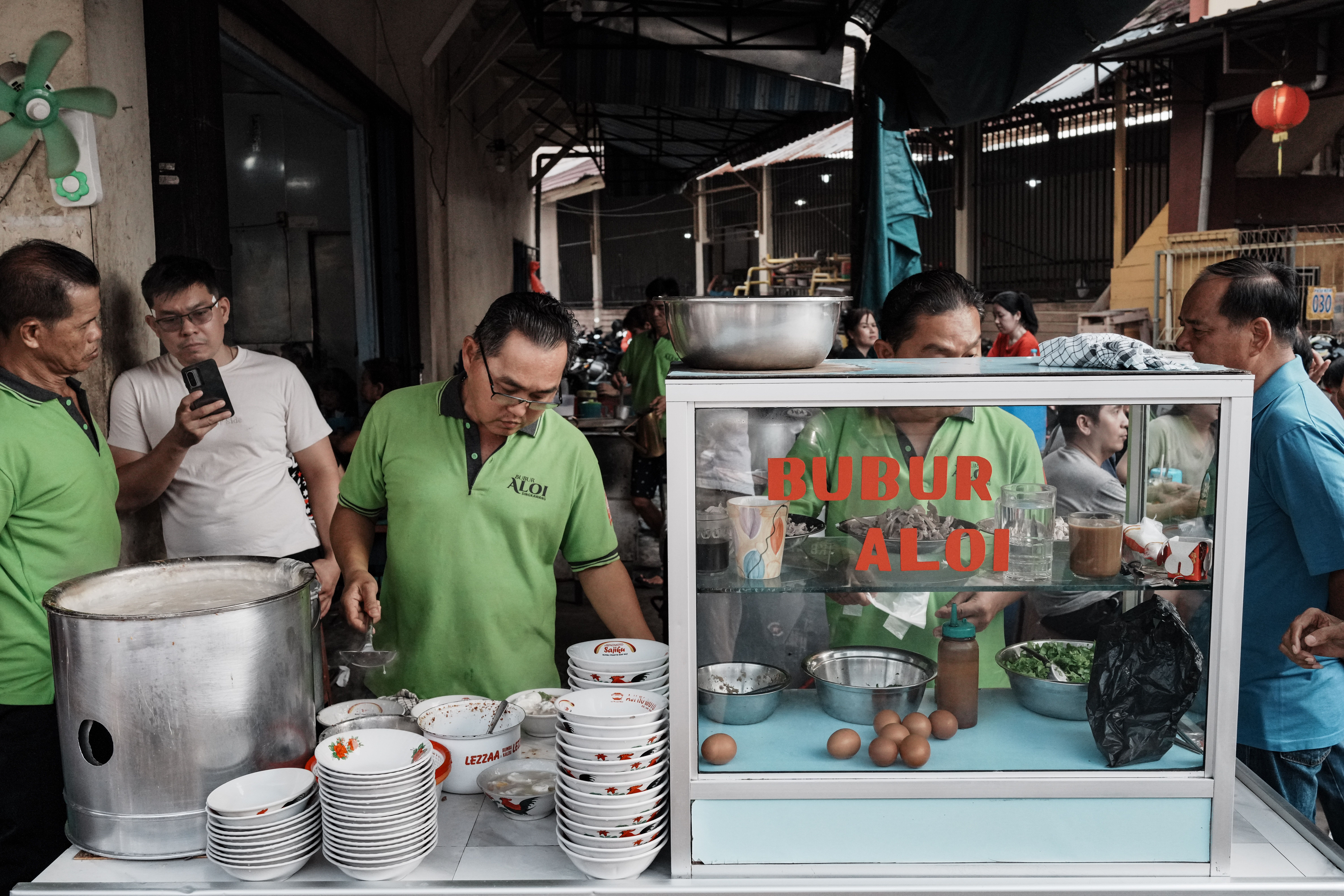 Bustling scene at a street food stall serving porridge in Singkawang, Indonesia.