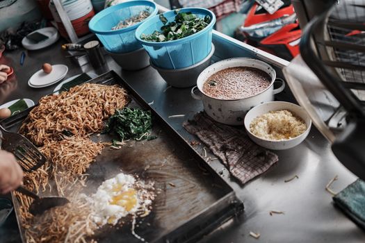 A close-up of street food preparation with noodles and eggs in Singkawang's bustling market.