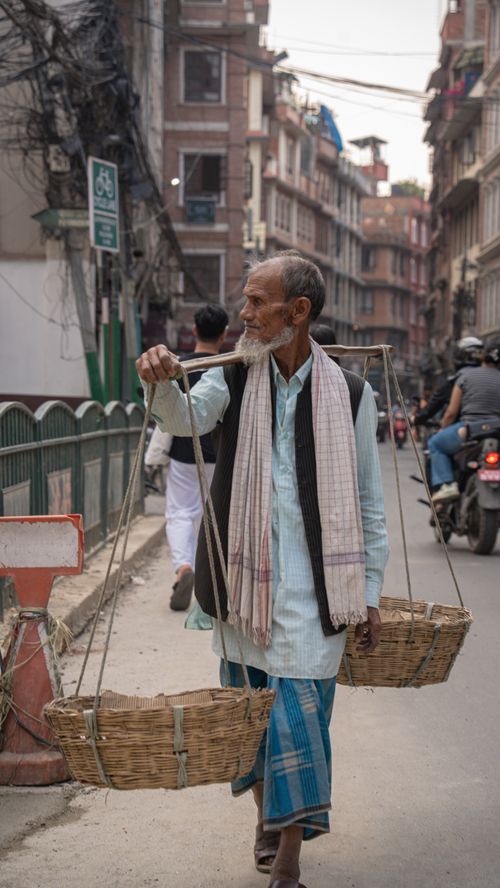 Free An elderly man carrying baskets on a street in Kathmandu, Nepal. Captures traditional lifestyle. Stock Photo