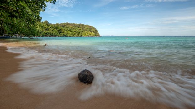 Scenic view of a tropical beach with clear water and lush green forest.