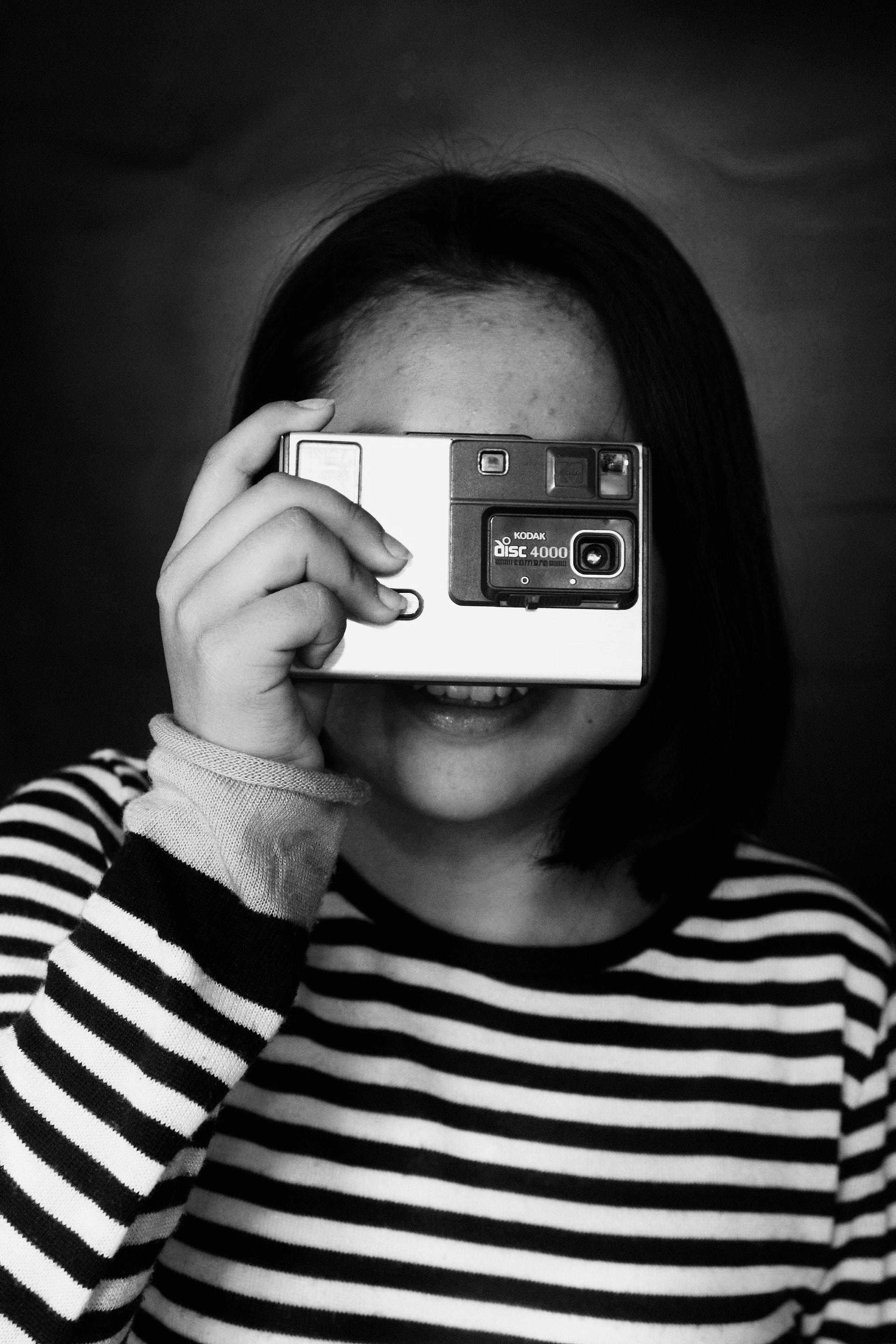 Portrait of a person holding a vintage film camera covering their face, symbolizing the historical connection between camera obscura and modern photography.