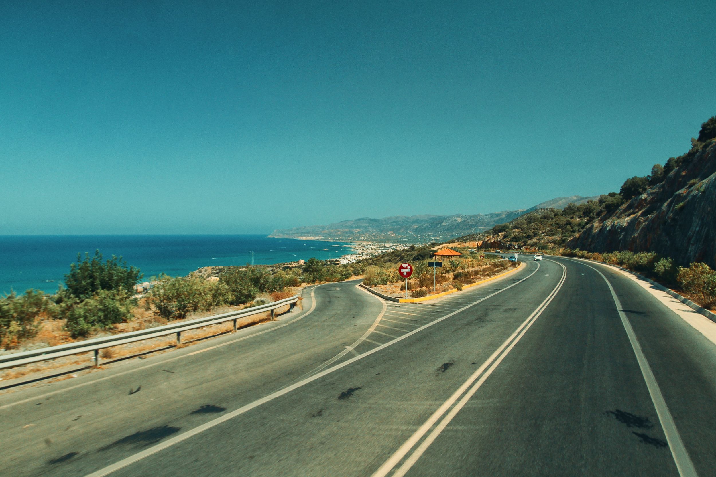 A winding road along the coast with a stunning ocean view under clear blue skies.