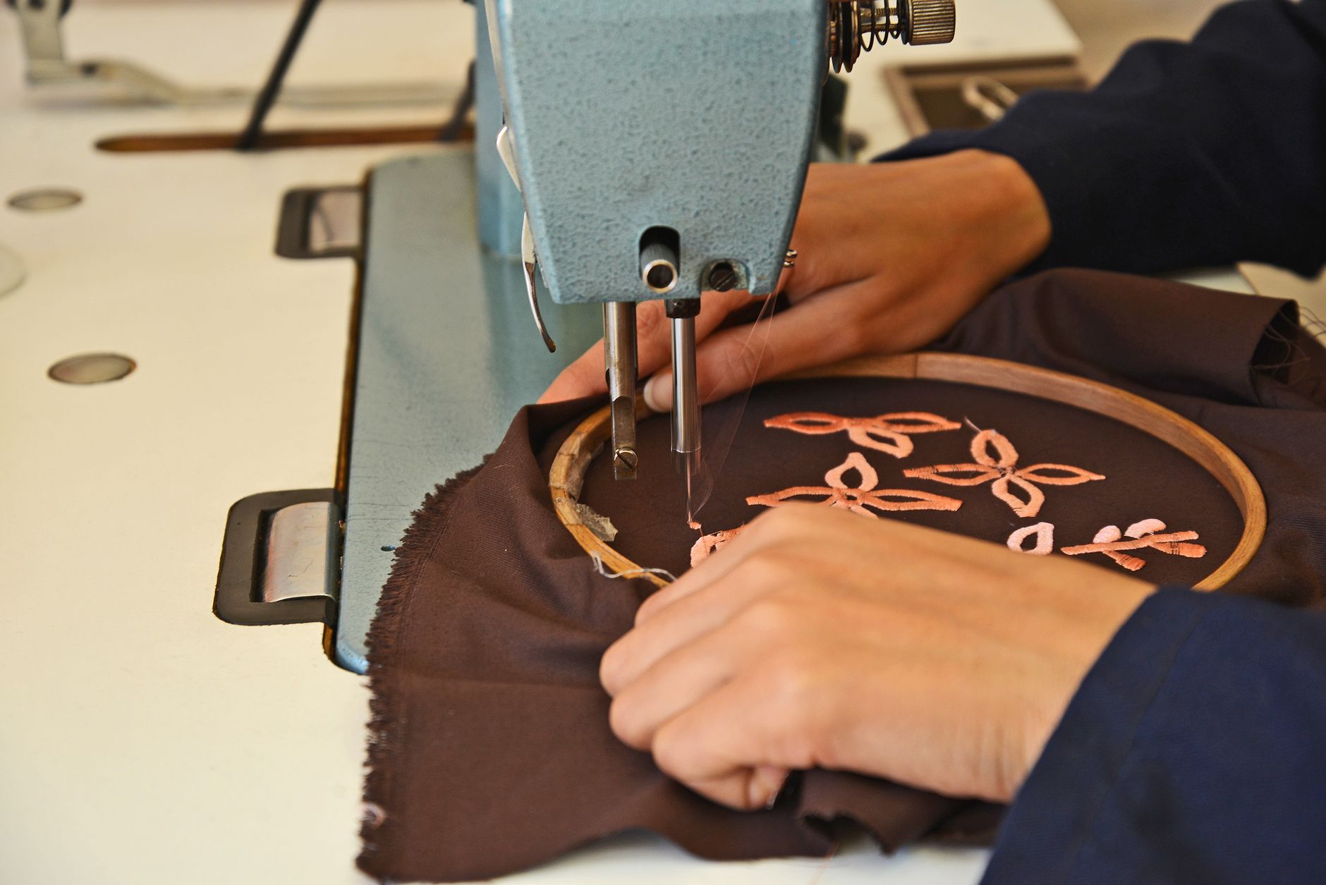 Broderie artisanale d'un motif floral au point de piqûre sur tissu, réalisée à l'aide d'une machine