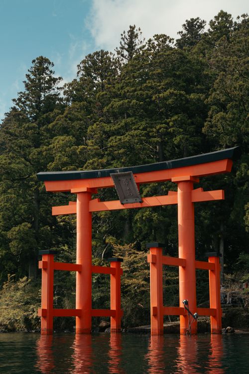 Free Stunning view of a traditional red torii gate on Lake Ashi, surrounded by lush forests in Hakone, Japan. Stock Photo