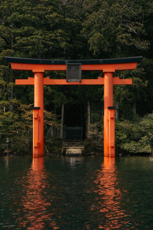 Free Beautiful torii gate reflecting on Lake Ashi with lush forest backdrop in Hakone, Japan. Stock Photo