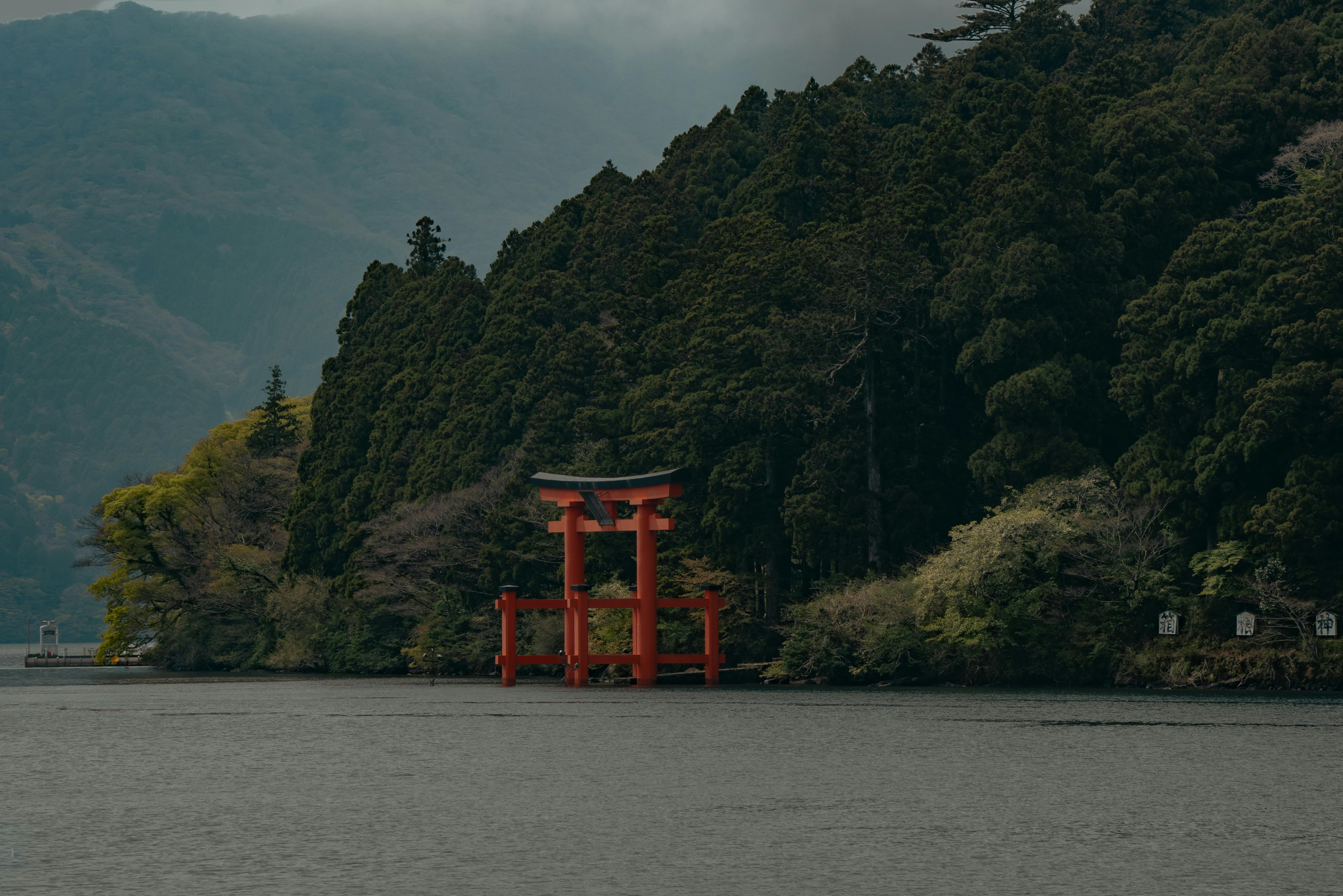 Peaceful scene of the red torii gate at Hakone Shrine by the lakeside amidst dense green forestry.