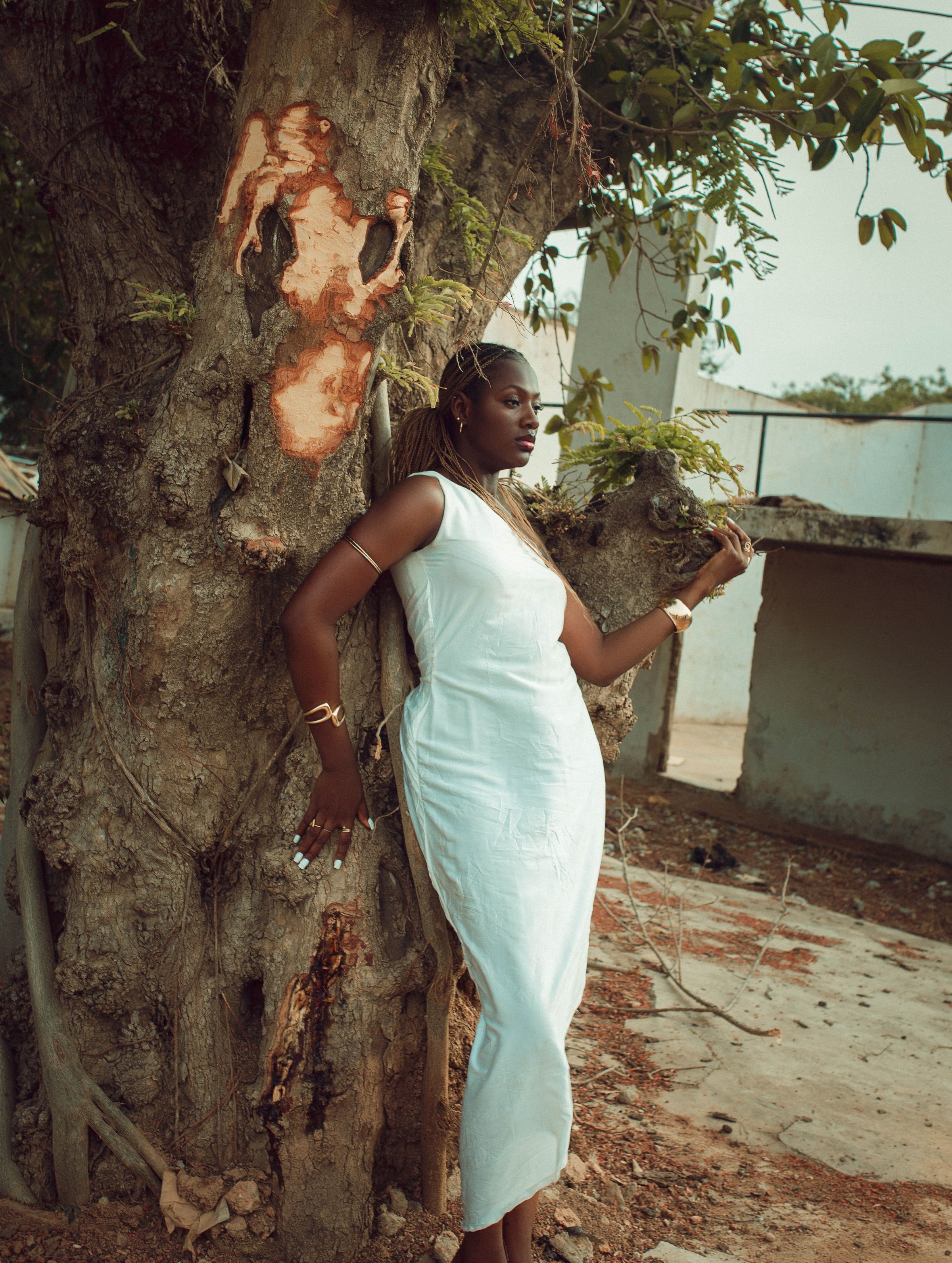 A woman in a long white dress against a tree in Zaria.