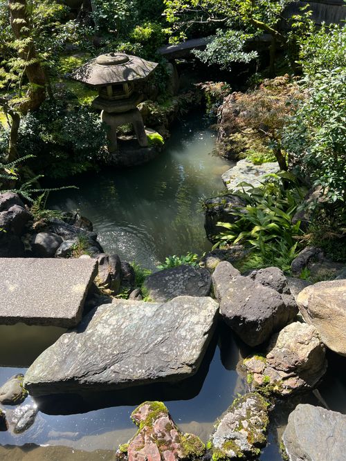 Free A tranquil Japanese garden featuring a stone lantern by a pond surrounded by lush green foliage. Stock Photo