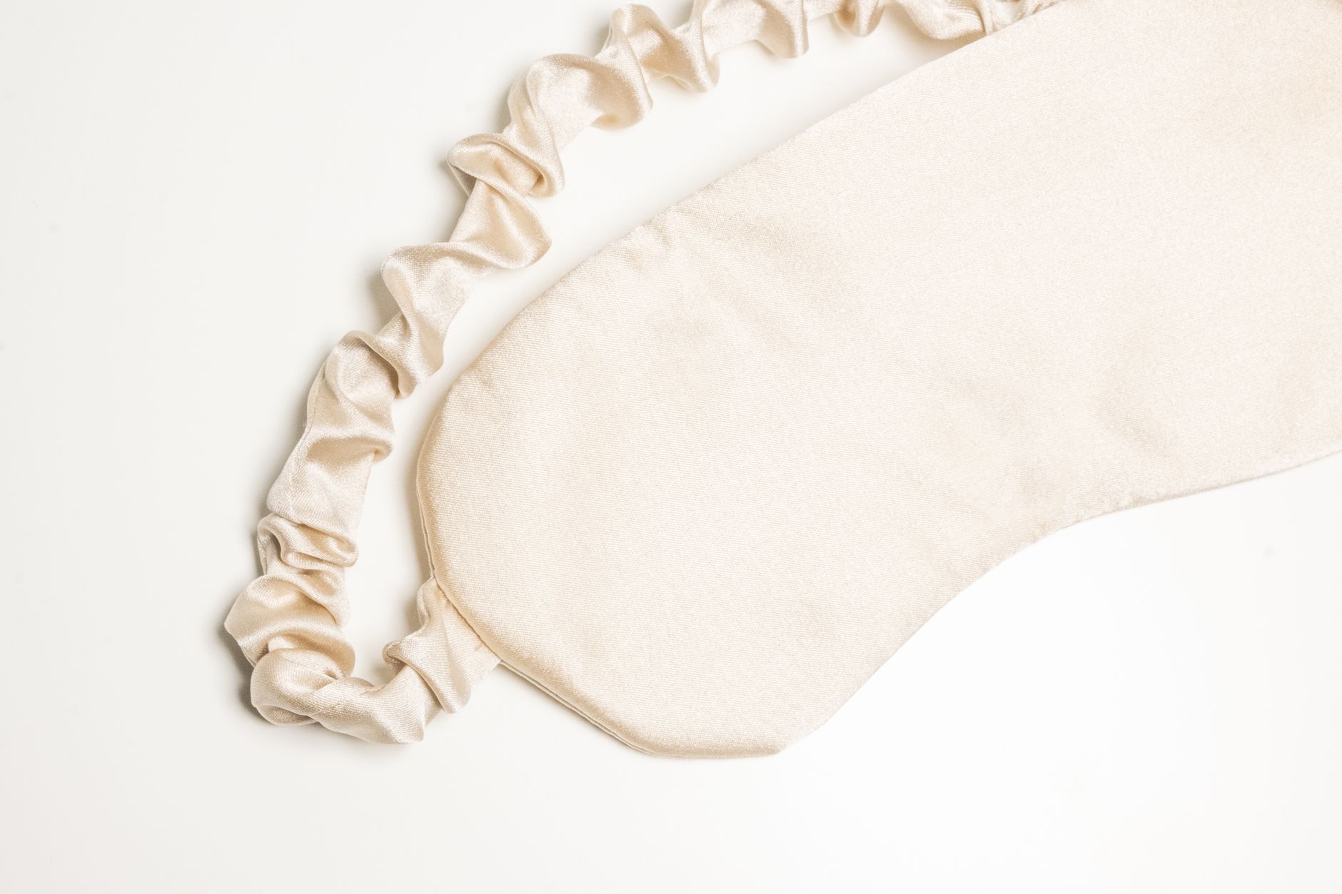 Elegant ivory silk sleep mask with ruched band, perfect for relaxation and beauty care.