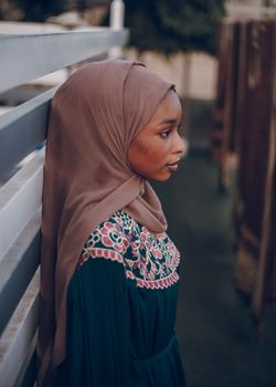 Side profile of a woman in a beautifully embroidered dress, wearing a hijab, standing outdoors.