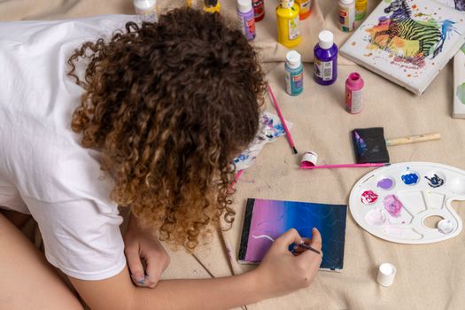 A young artist paints with acrylics on a canvas surrounded by supplies, showcasing creativity.