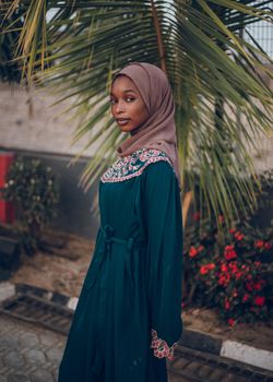 Elegant young woman in traditional attire standing gracefully outdoors with lush background.