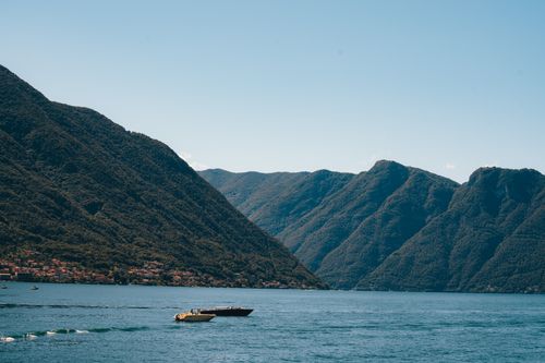 Free Tranquil scene of Lake Como with boats and lush green mountains under a clear blue sky. Stock Photo