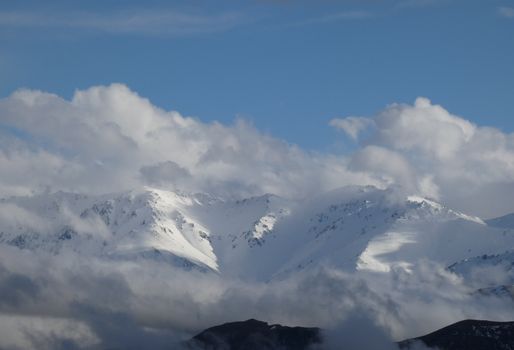 Beautiful view of snow-capped mountains surrounded by clouds against a bright blue sky.