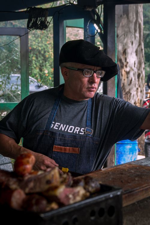 Free Chef wearing a beret prepares meat at an outdoor food stand, creating a rustic and authentic culinary scene. Stock Photo