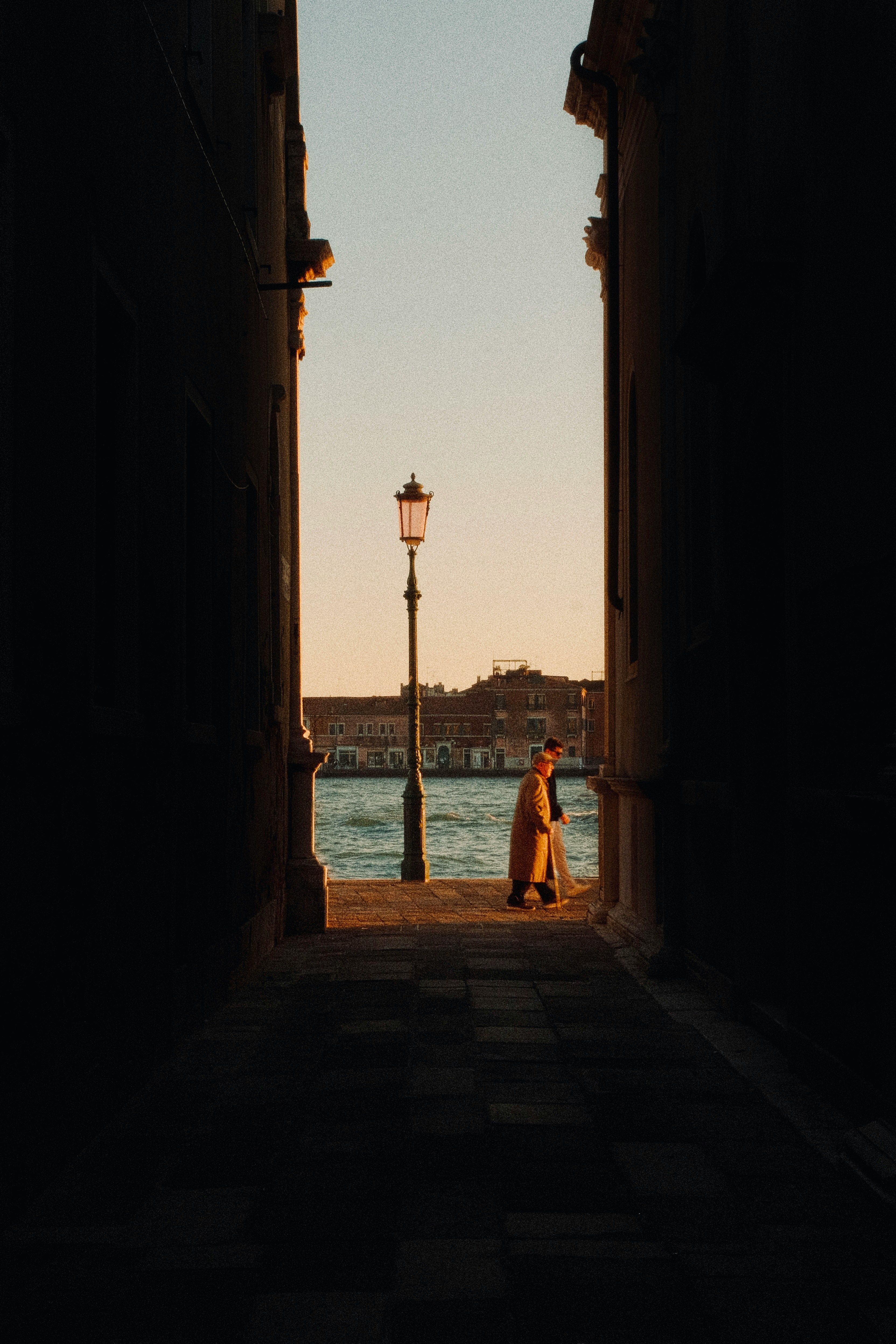 Person walking in a Venetian alleyway at sunset, with a view of a canal and historic architecture.
