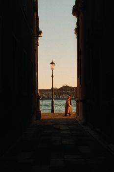 Person walking in a Venetian alleyway at sunset, with a view of a canal and historic architecture.