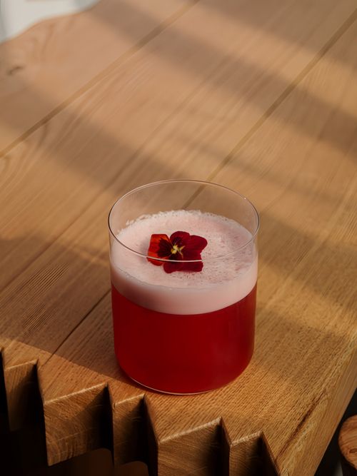 Free A vibrant red cocktail with a flower garnish in a transparent glass on a wooden table. Stock Photo