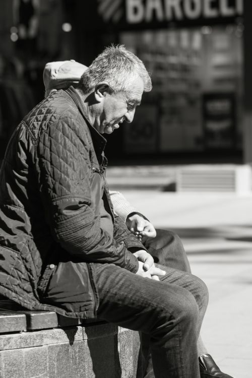 Free A contemplative older man sitting outdoors, captured in black and white. Stock Photo