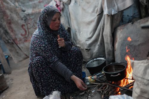 Free A woman in traditional attire cooks over an open fire outdoors, evoking resilience. Stock Photo