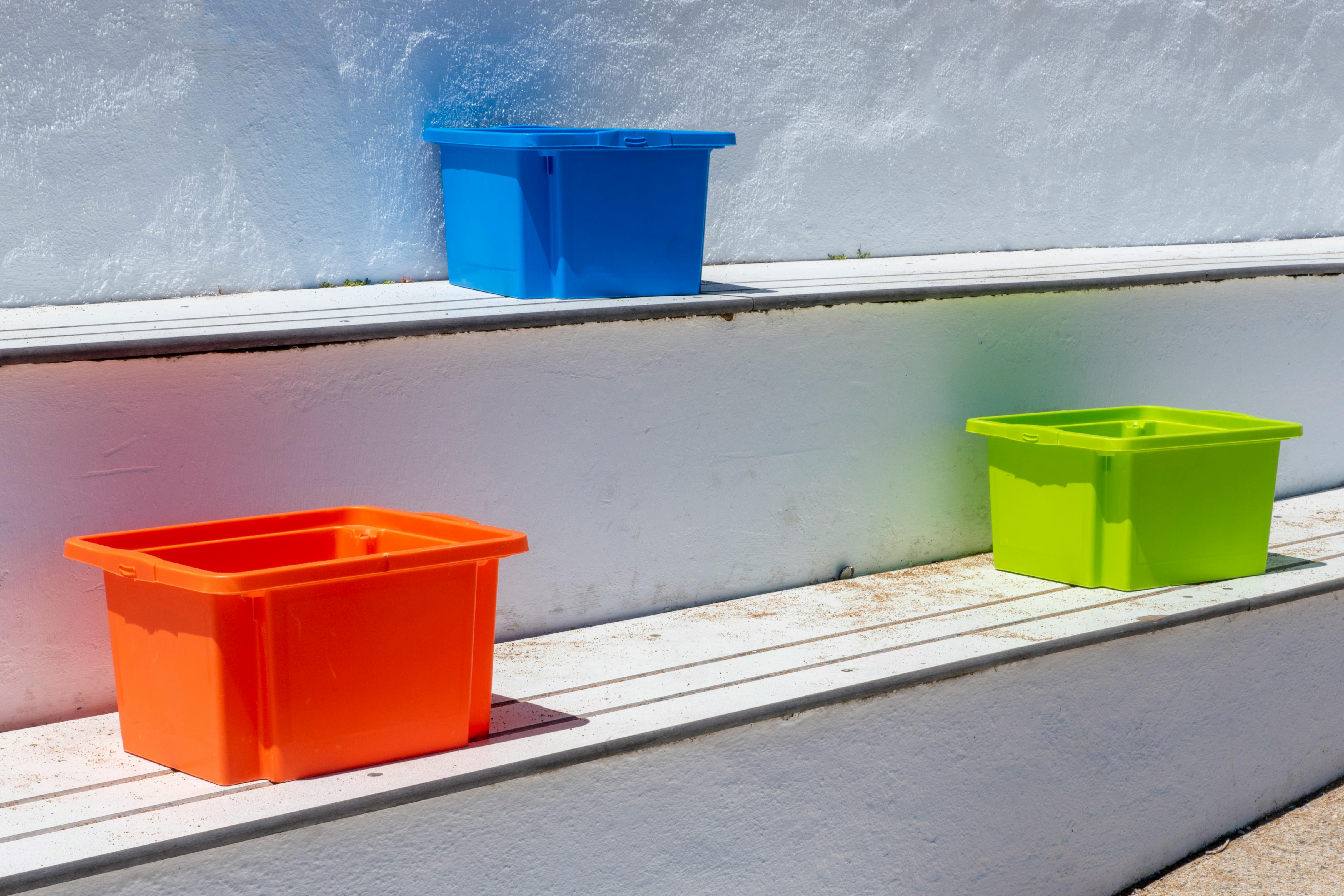 屋外の階段に置かれた、色鮮やかなプラスチック製の収納ボックス。日差しが当たっている。