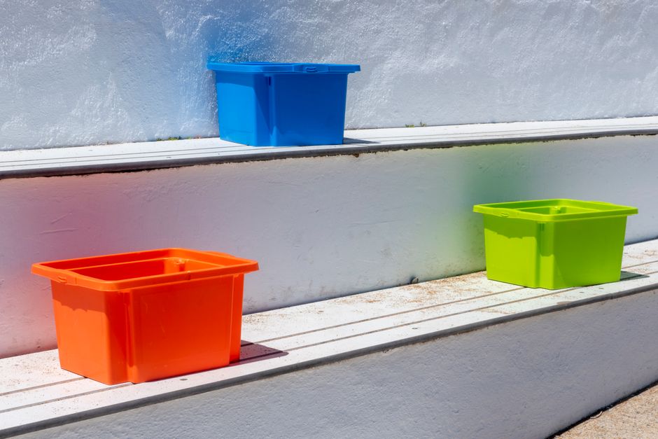 屋外の階段に置かれた、色鮮やかなプラスチック製の収納ボックス。日差しが当たっている。