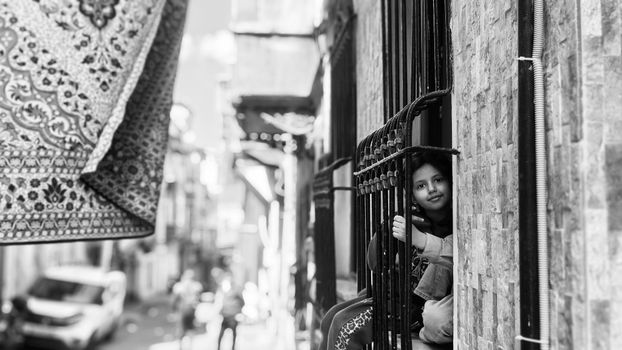 Young girl peering out from an İstanbul window, adding charm to the bustling street below.
