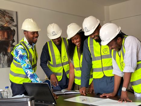 Diverse team of African engineers in hard hats and safety vests reviewing building plans indoors.