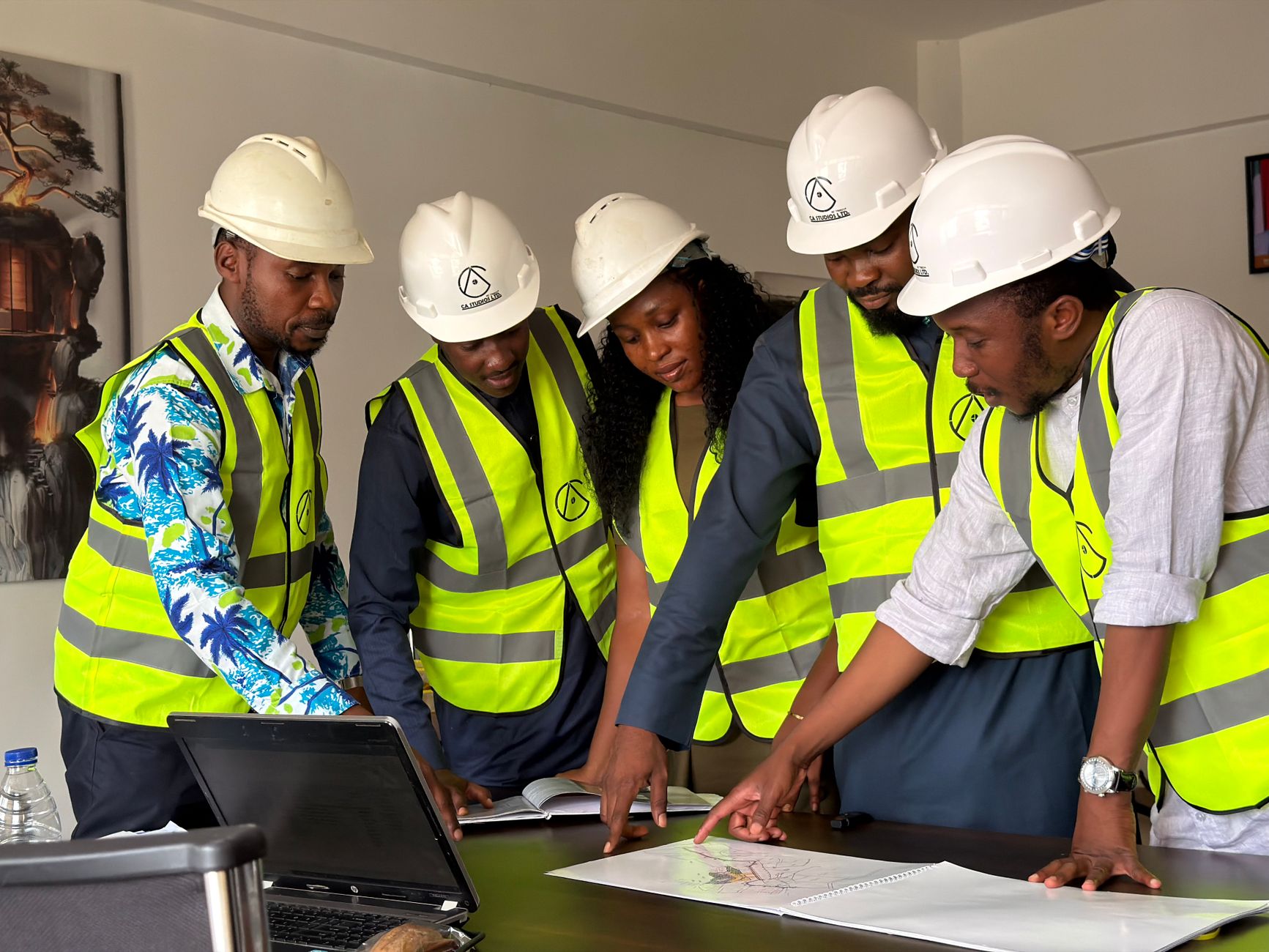 A diverse team of five engineers in safety gear examines construction plans indoors.