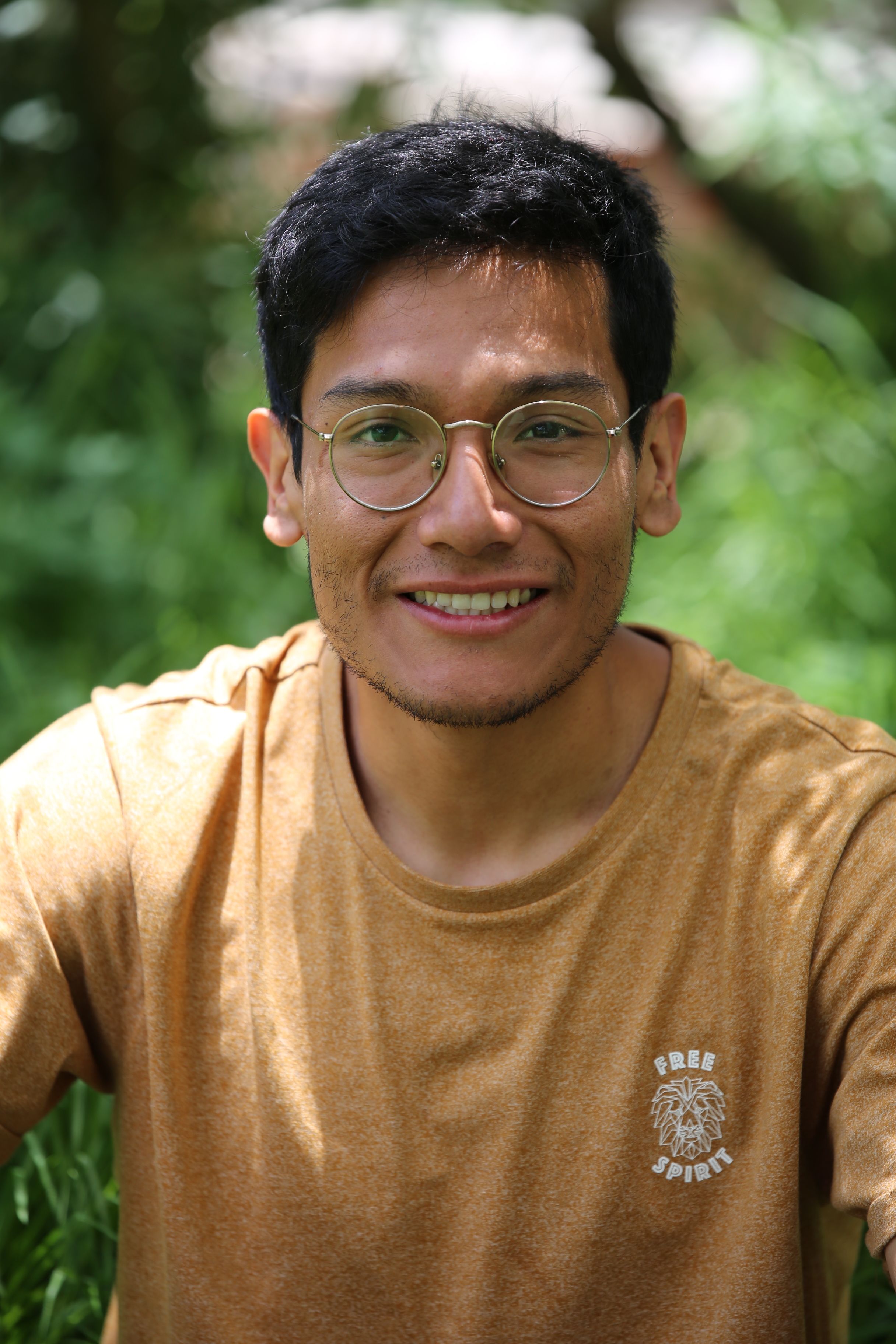 Portrait of a smiling man wearing glasses in an outdoor green setting.