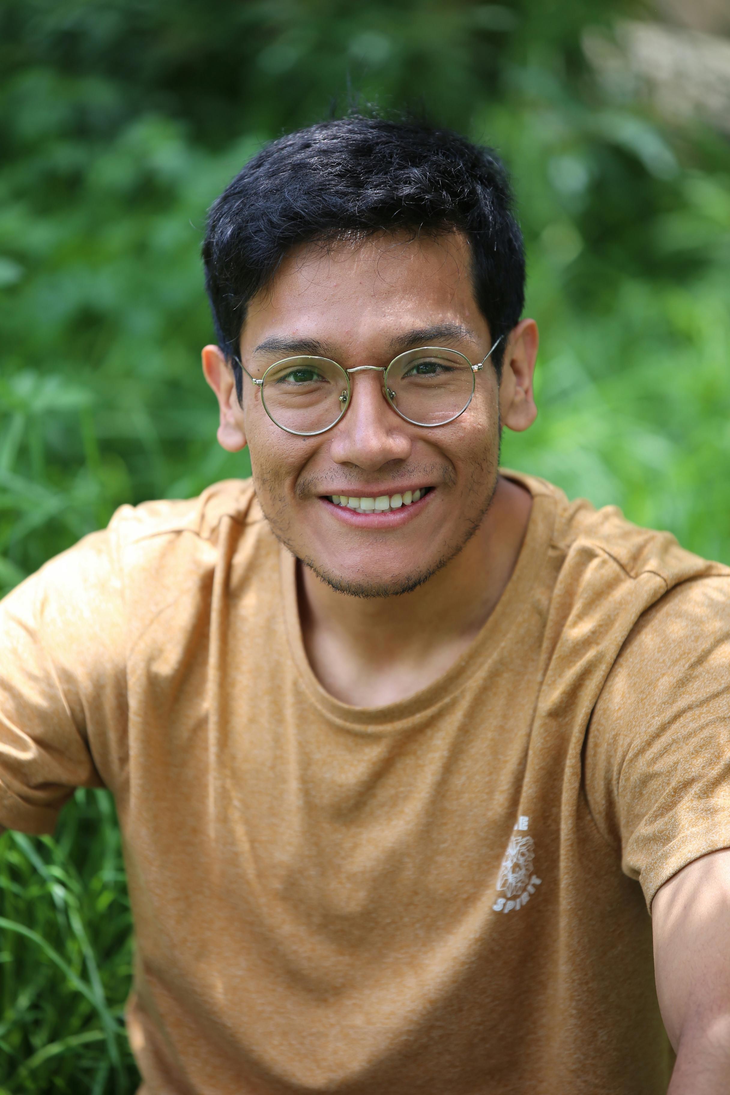Portrait of a smiling young man wearing glasses with a nature background.