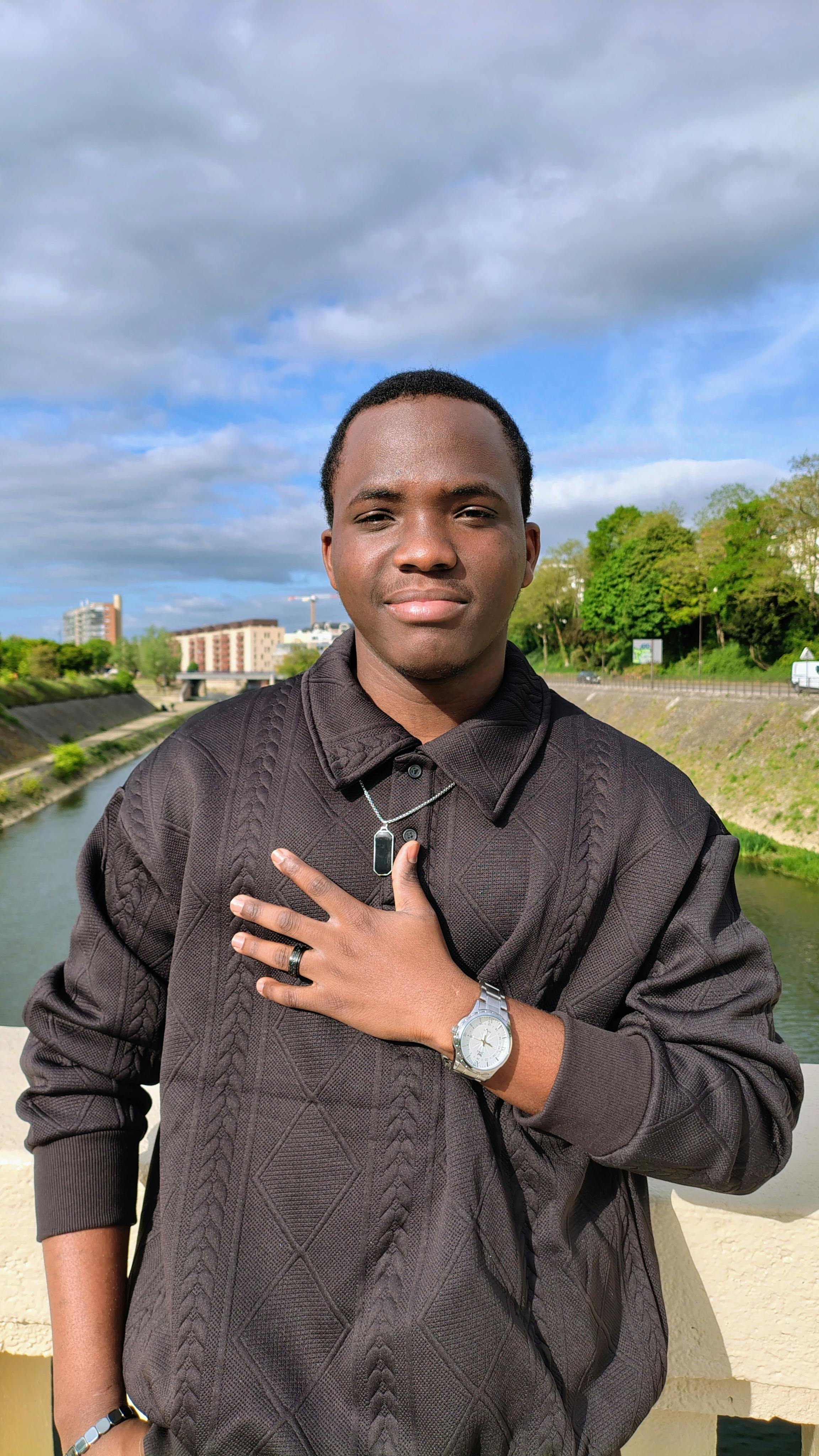Confident young adult standing on a bridge in an urban setting with scenic views.