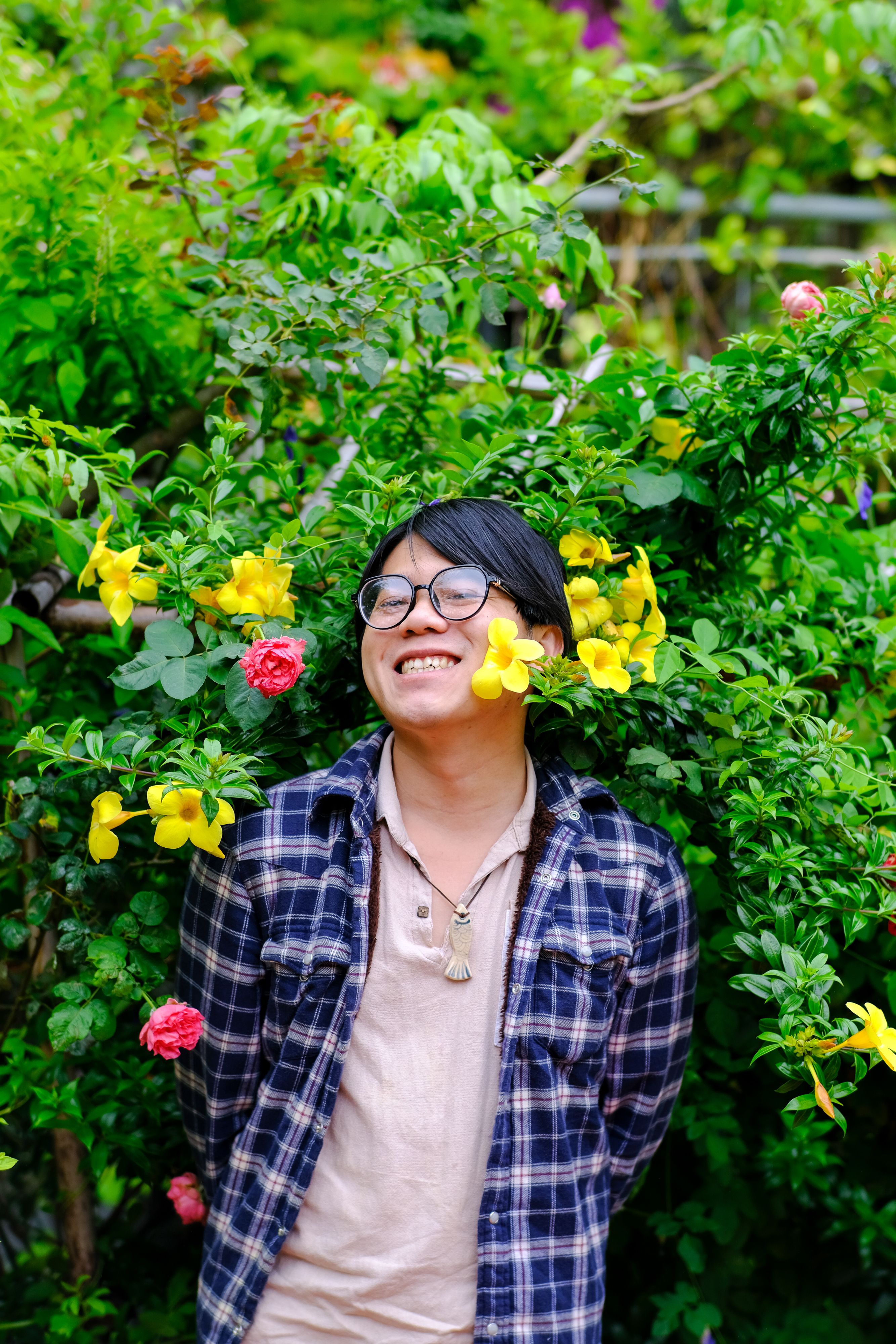Happy young man surrounded by lush flowers and greenery in Hue, Vietnam. Captures nature's vibrant beauty.