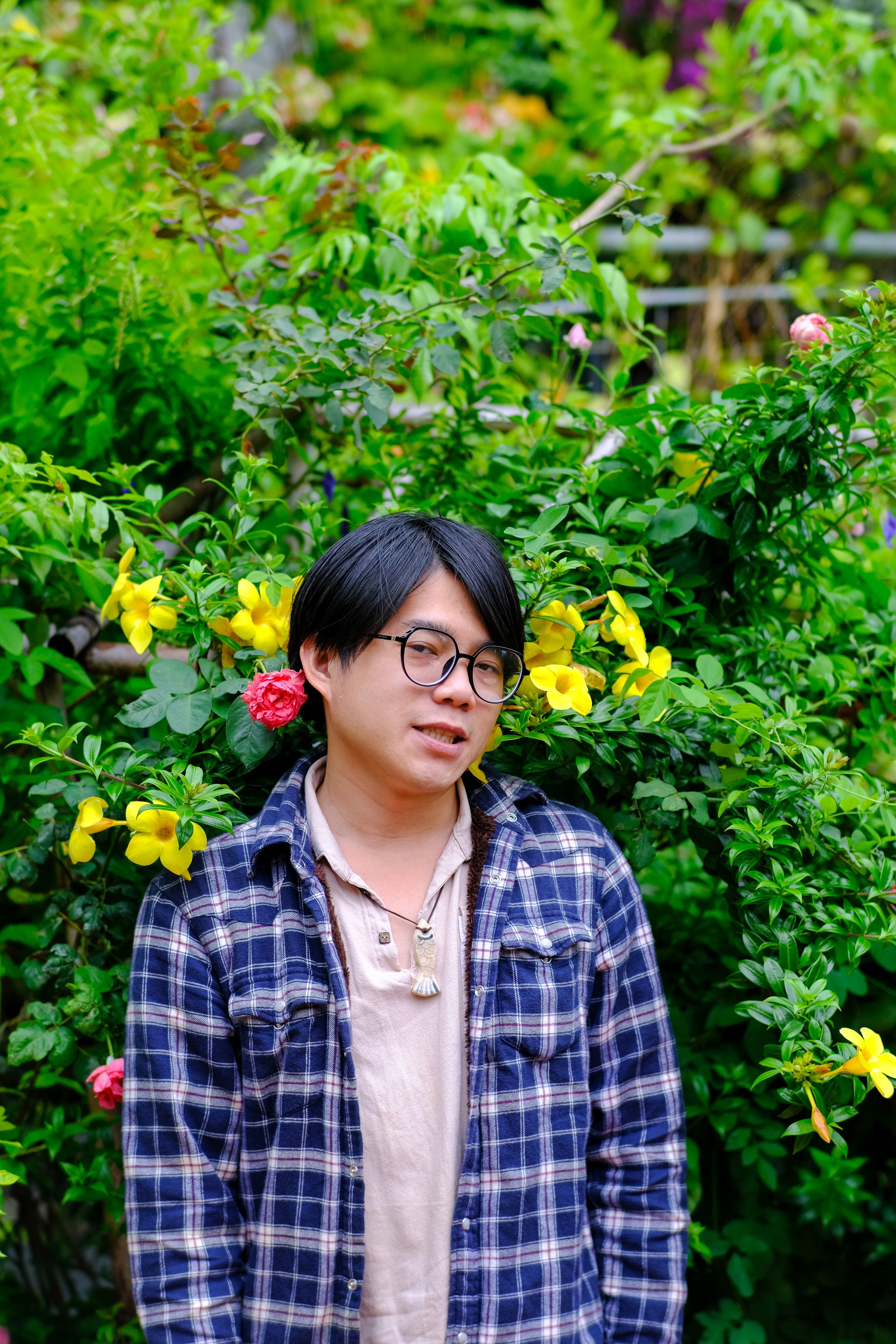 A man stands against a vibrant garden backdrop in Hue, Vietnam, showcasing personal style.