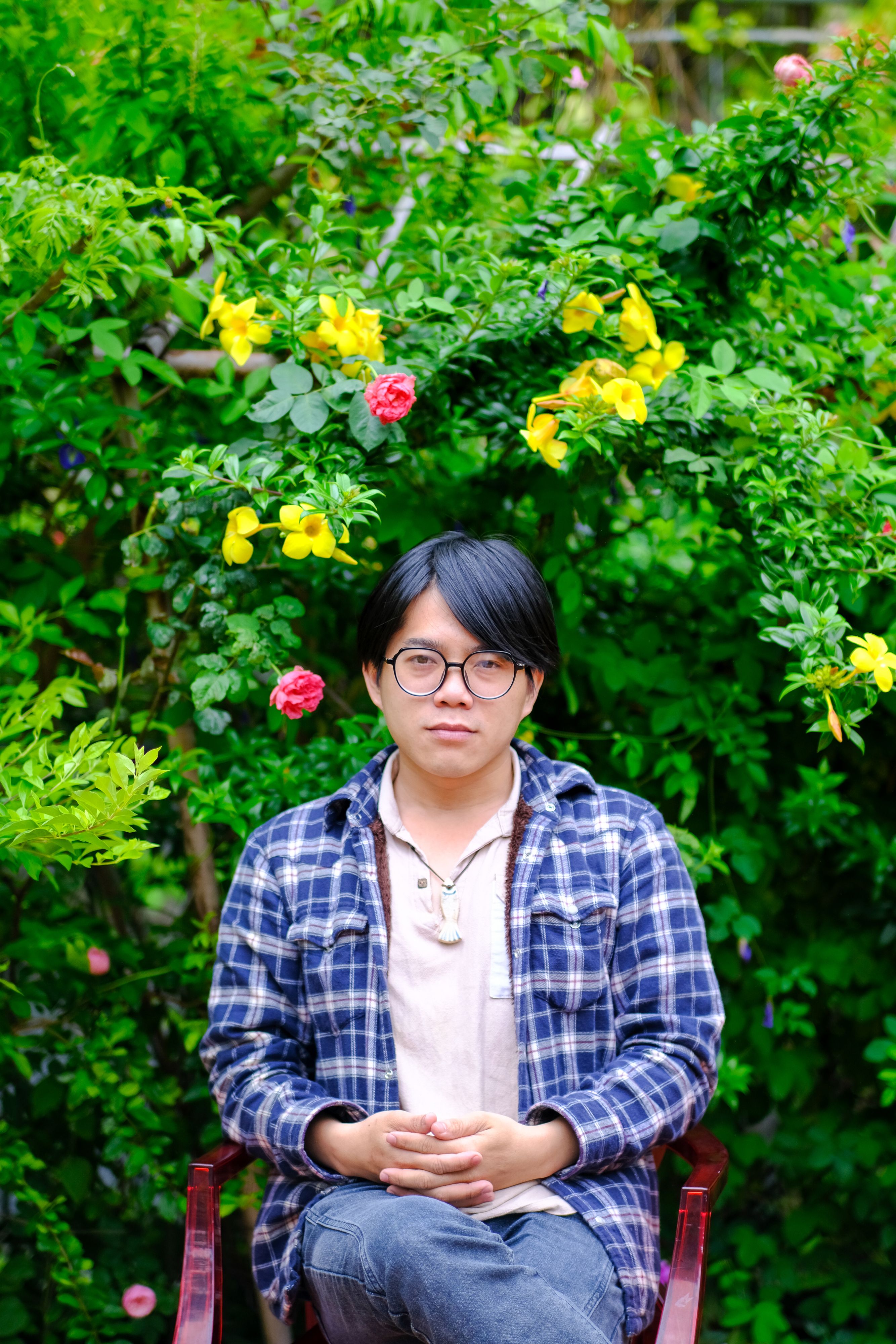 A serene portrait of a man seated in a lush, flower-filled garden in Hue, Vietnam.