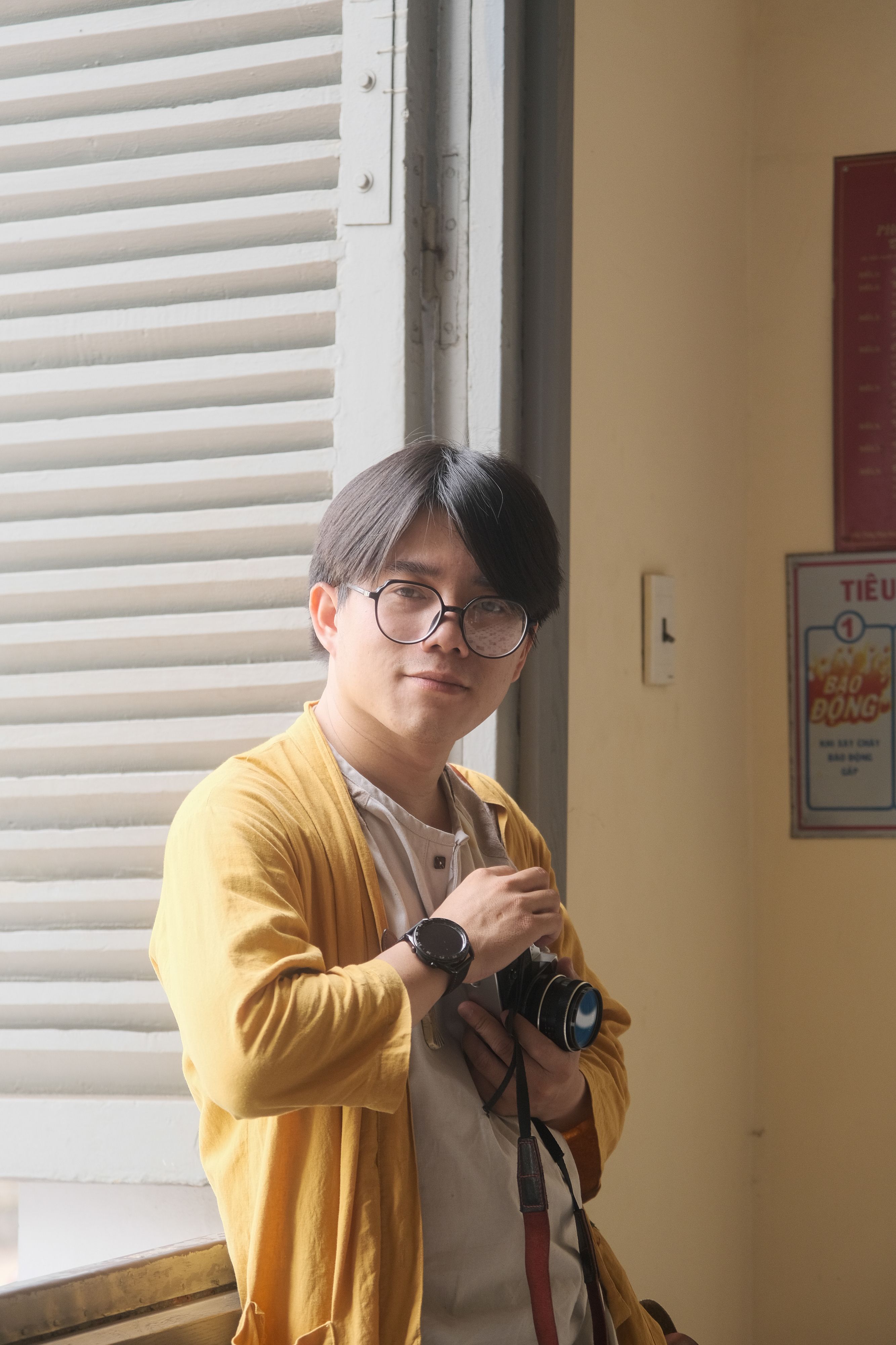 A young person holding a camera by a window in Hue, Vietnam.