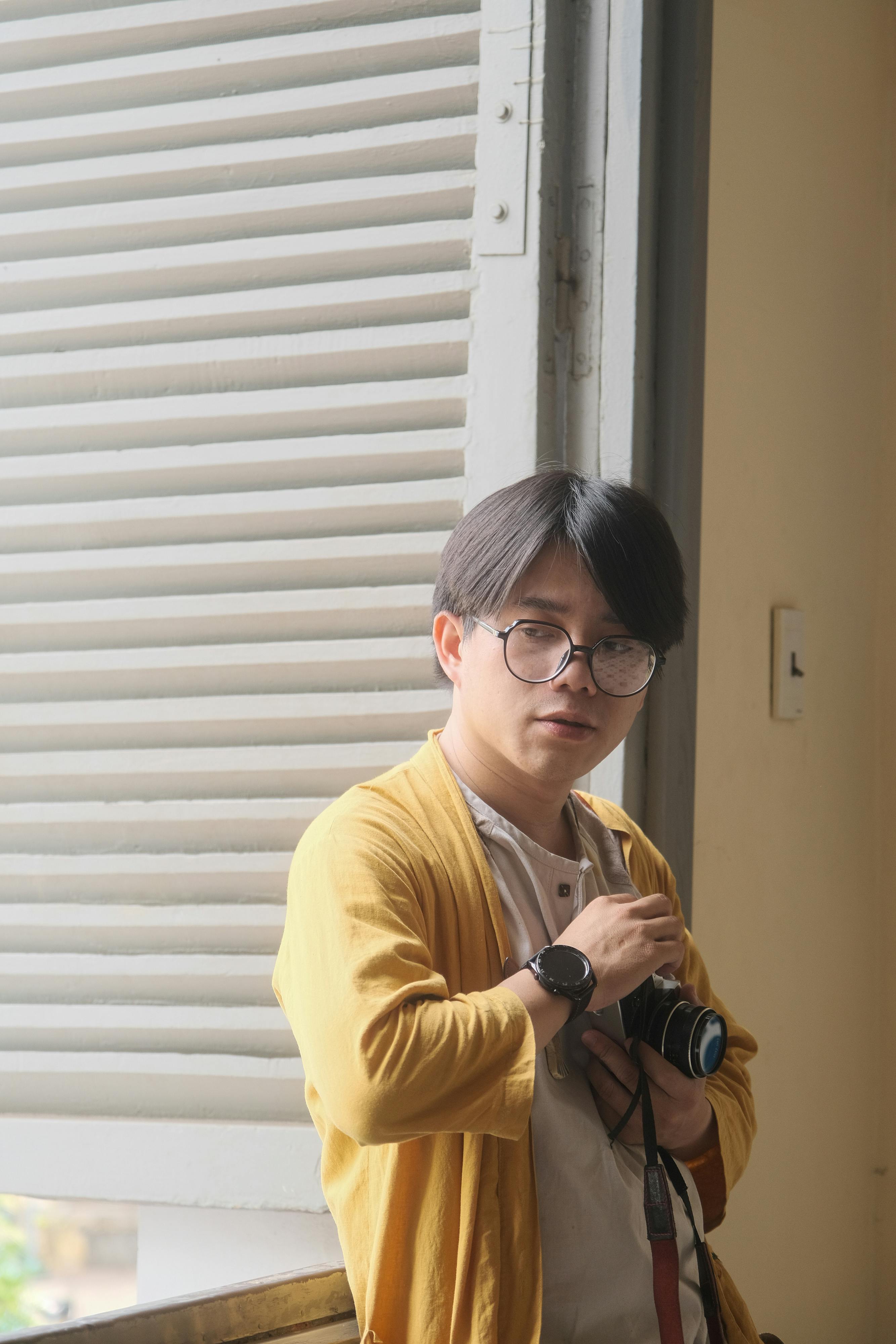 A thoughtful man in Hue, Vietnam, captured with a camera in hand indoors.