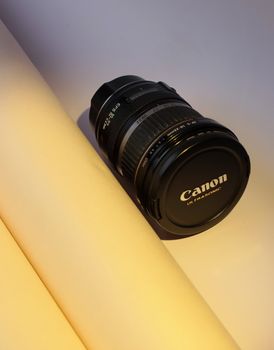 Close-up of a Canon camera lens placed on a light-colored artistic background.