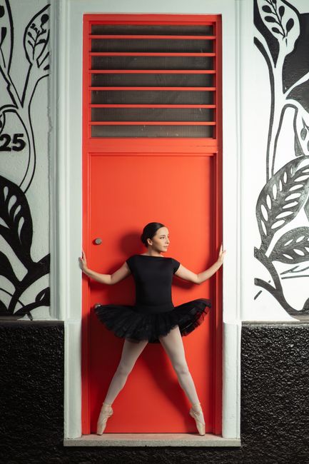 Elegant ballet dancer in black tutu striking a pose against a vibrant red door with artistic decor.
