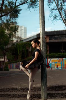 Ballet dancer in elegant pose outdoors with urban backdrop, showcasing grace and balance.
