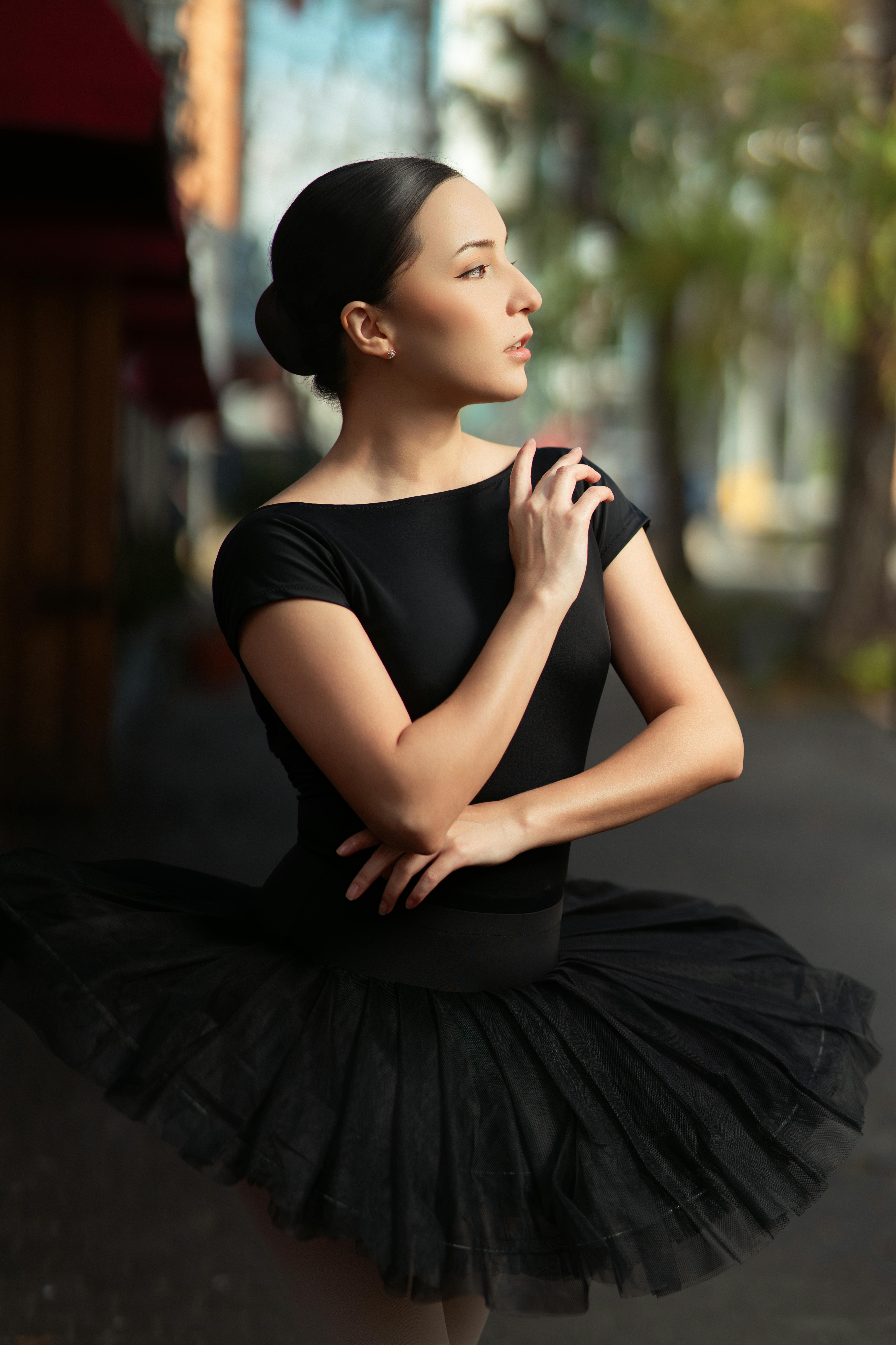 A ballerina in a black tutu strikes a graceful pose on an outdoor street, exuding elegance.