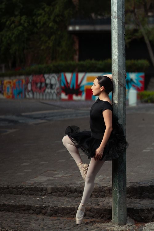 Free Ballerina in black tutu poses elegantly by a colorful street art wall, merging dance with urban scenery. Stock Photo
