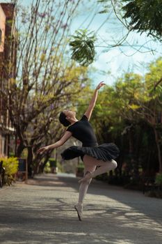 Ballet dancer gracefully leaps in an outdoor setting, wearing a black tutu.