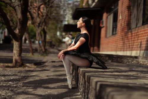 Free Elegant ballerina sitting gracefully outdoors in urban environment. Stock Photo